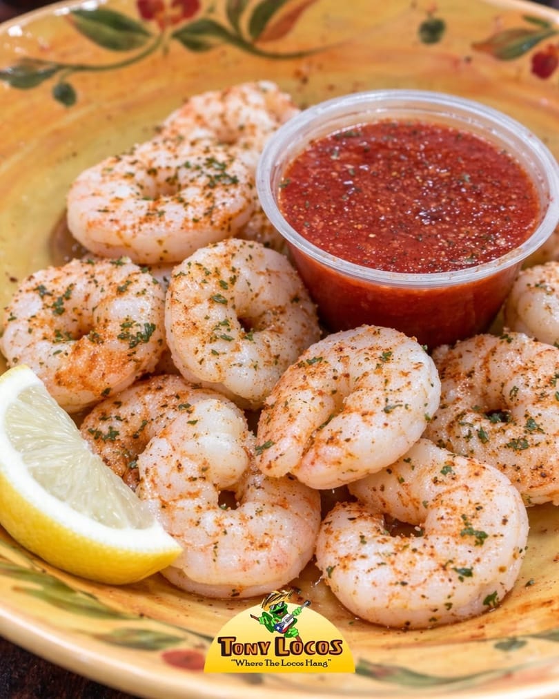 Tony Locos' seasoned shrimp with a lemon wedge and a side of red dipping sauce.