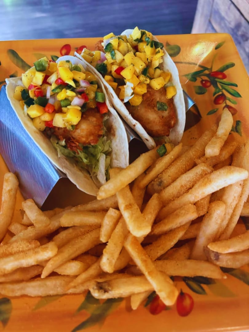 Two fish tacos with mango salsa and a side of french fries on a decorative orange plate.