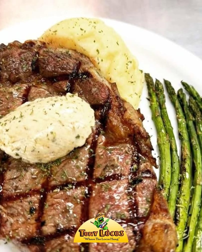 Grilled steak with a dollop of butter, mashed potatoes, and asparagus on a white plate.