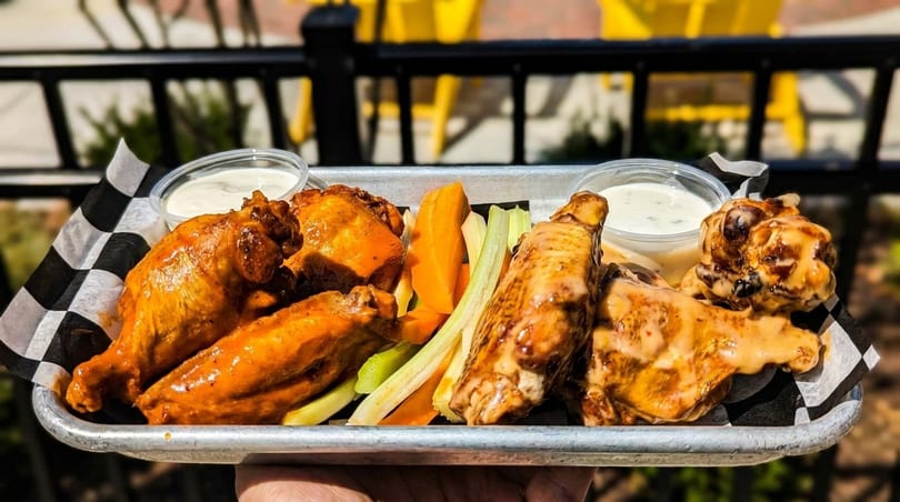 A metal tray of buffalo wings, carrots, celery, and dipping sauces, held outdoors.